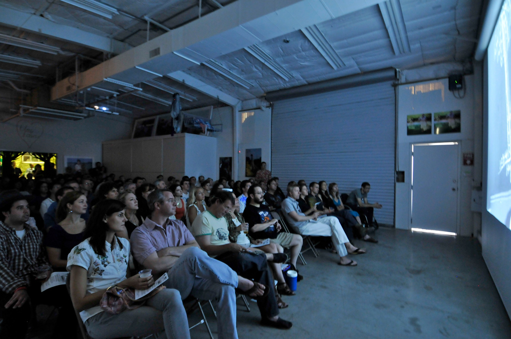 An audience in a warehouse-like space watching a film screening.