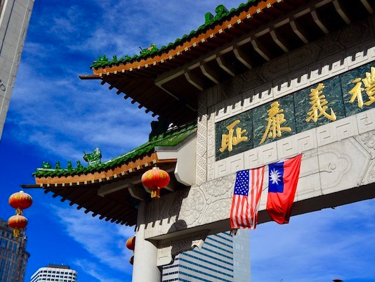 Photo of a Chinese-style gate with eaves curling up. There are lanterns, as well as an American and Taiwanese flag hanging from it.